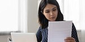Attentive millennial Asian female holding paper letter document reading