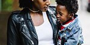 Black woman holding a toddler and walking down a city street.